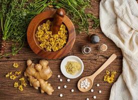 oben Aussicht homöopathisch Tabletten im ein hölzern Löffel und Flaschen mit das Kraut im ein Granatwerfer mit ein Stößel auf hölzern Tabelle Hintergrund foto