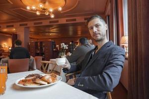 Mann mit Kaffee und Frühstück Sitzung beim Essen Tabelle im Luxus Hotel foto