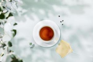 Tasse von Tee mit Papier Tee Taschen auf Blau Hintergrund mit Grün Blätter foto