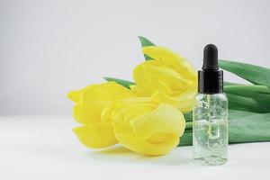 kosmetisch Serum auf ein Licht Hintergrund mit drei Gelb Tulpen foto