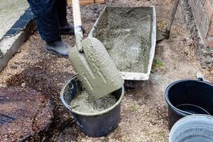 Arbeiter setzt Beton im Eimer mit Schaufel foto