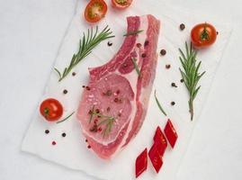 roh Schweinefleisch Filet auf das Knochen und Gewürze auf ein Weiß Hintergrund. Portion zum Mittagessen und Abendessen, oben Aussicht foto