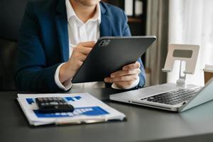 Geschäftsfrau, die vorne Tablet, Laptop-Computer mit Finanzdiagrammen und Statistiken auf monitor.at-Büro sitzt foto