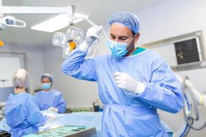 Porträt von männlich Arzt der Chirurg nehmen aus medizinisch Maske Stehen im Betrieb Zimmer. der Chirurg beim modern Betriebs Zimmer foto