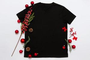 Schließen Sie herauf schwarzes leeres Schablonent-shirt mit Kopienraum und Weihnachtsfeiertagskonzept. Draufsichtmodellt-shirt und rote Feiertagsdekorationen auf weißem Hintergrund. frohes neues jahr zubehör. Weihnachts-Outfit foto