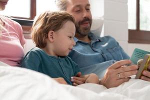 wenig Jungs Vater lesen Geschichten zu Kinder Vor gehen zu Bett zu entspannen und Schlaf solide bis um das Morgen. foto