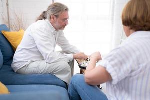 im das Leben Zimmer von das Haus, ein Alten Paar sitzt und entspannt. zu Start spielen Schach zusammen mit ein Schach Tafel. foto