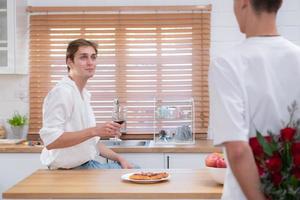 ein jung lgbt Paar feiert das Tag von Liebe mit ein Glas von Wein im ihr Zuhause Küche. mit ein Überraschung mit ein Rose von ein Liebhaber foto