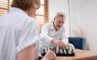 im das Leben Zimmer von das Haus, ein Alten Paar sitzt und entspannt. zu Start spielen Schach zusammen mit ein Schach Tafel. foto
