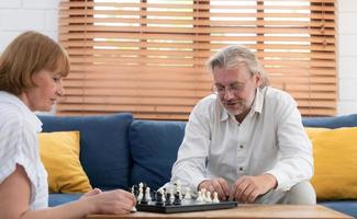 im das Leben Zimmer von das Haus, ein Alten Paar sitzt und entspannt. zu Start spielen Schach zusammen mit ein Schach Tafel. foto