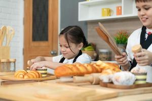 Porträt von ein wenig Mädchen und Junge im das Küche von ein Haus haben Spaß spielen Backen Brot foto