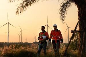 Ingenieure Arbeiten auf Wind Bauernhöfe zum verlängerbar Energie sind verantwortlich zum Aufrechterhaltung groß Wind Turbinen. Rückkehr von Arbeit während während das Abend Sonne scheint ein schön golden Licht auf beide von foto