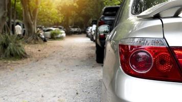 Rückseite Aussicht von ein Auto im ein Wohn Parkplatz viel. sichtbar Rückleuchten von Silber Auto und verschwommen von Spiegel Flügel. lange Reihe von Autos geparkt im ruhig Nachbarschaft. verschwommen von Schatten von hoch Bäume neben Straße. foto