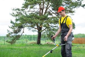 ein männlich Gärtner mäht das Grün Gras von das Rasen im das Hinterhof mit ein Benzin Mäher. Trimmer zum das Pflege von ein Garten Handlung foto