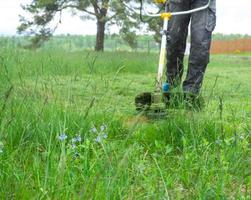 ein männlich Gärtner mäht das Grün Gras von das Rasen im das Hinterhof mit ein Benzin Mäher. Trimmer zum das Pflege von ein Garten Handlung foto