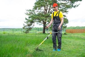 ein männlich Gärtner mäht das Grün Gras von das Rasen im das Hinterhof mit ein Benzin Mäher. Trimmer zum das Pflege von ein Garten Handlung foto