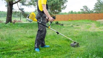 ein männlich Gärtner mäht das Grün Gras von das Rasen im das Hinterhof mit ein Benzin Mäher. Trimmer zum das Pflege von ein Garten Handlung foto