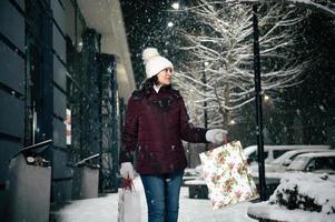 herrlich jung Frau Gehen Nieder das Straße mit Einkaufen Taschen mit Weihnachten Geschenk Box im ihr Hände. fröhlich Weihnachten. foto