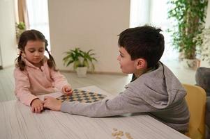 zwei bezaubernd europäisch elementar alt Kinder, Junge und Mädchen, Bruder und Schwester haben großartig Zeit spielen Dame Tafel Spiel zusammen beim Zuhause Innere foto