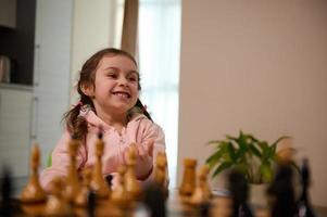 bezaubernd wenig kaukasisch Mädchen spielen Schach Spiel beim heim. Clever intellektuell Tafel Spiele zum Kinder, Logik Entwicklung, Bildung Konzept foto