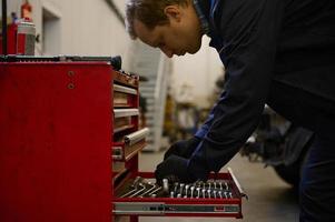 Seite Porträt von ein Auto Mechaniker nehmen Schlüssel von das Box im das Reparatur Geschäft Garage. Garantie Reparatur und Auto Instandhaltung Konzept foto