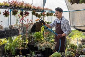 asiatisch Gärtner ist Bewässerung das saftig Pflanze Innerhalb seine Gewächshaus mit Schlauch zum Hobby und Zier Garten Geschäft Konzept foto