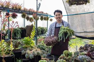 asiatisch Gärtner ist Arbeiten Innerhalb das Gewächshaus voll von saftig Pflanzen Sammlung während halten einer gesund Topf zum Zier Garten und Freizeit Hobby Konzept foto