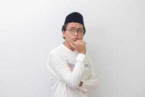 Porträt von jung asiatisch Muslim Mann Denken Über Frage mit Hand auf kinn. isoliert Bild auf Weiß Hintergrund foto