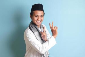 Porträt von asiatisch Muslim Mann im Weiß koko Hemd tun kriegerisch Kunst Geste oder pencak Silat. isoliert Bild auf Blau Hintergrund foto