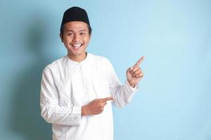 Porträt von jung asiatisch Muslim Mann zeigen Produkt und zeigen mit seine Hand und Finger zu das Seite. isoliert Bild auf Blau Hintergrund foto