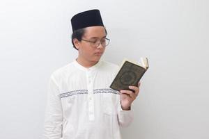 Porträt von jung asiatisch Muslim Mann lesen und rezitieren heilig Buch von Koran ernsthaft. isoliert Bild auf Weiß Hintergrund foto