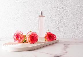 ein elegant Flasche von Damen Parfüm oder Eau de Toilette steht auf ein dekorativ Tablett mit Leben Rosa Rosen. ein Vorlage zum Werbung ein Produkt. foto