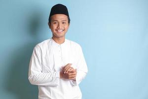 Porträt von asiatisch Muslim Mann im Weiß koko Hemd Gefühl zuversichtlich, lächelnd und suchen beim Kamera. isoliert im Blau Hintergrund foto