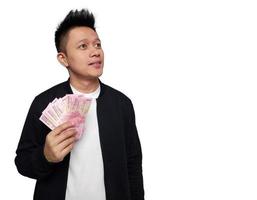 jung Mann mit hoffnungsvoll Gesichts- Ausdruck suchen oben und halten indonesisch Geld foto