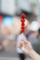 Frau Hand halten Karamell beschichtet Erdbeere Spieß beim Nacht Markt. Straße Essen und Reise Konzept foto