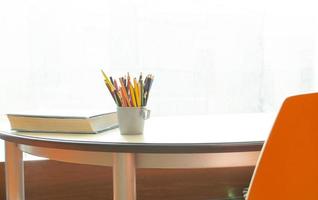 ein Tasse mit Bleistifte und ein Ecke von das Buch auf das Tabelle durch das Fenster. verschwommen Hintergrund. Arbeitsplatz zum lernen. leicht Zimmer. foto