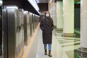 Eine Frau in einer medizinischen Gesichtsmaske wartet auf einen ankommenden Zug in der U-Bahn foto