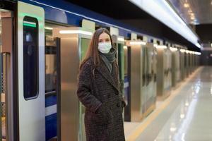 Ein Mädchen in einer chirurgischen Gesichtsmaske hält soziale Distanz zu einer U-Bahnstation foto