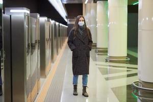 Eine Frau in einer medizinischen Gesichtsmaske wartet auf einen ankommenden Zug in der U-Bahn foto