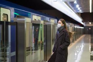 Eine Frau in einer medizinischen Gesichtsmaske wartet auf einen ankommenden Zug in der U-Bahn foto