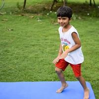 asiatisch Clever Kind tun Yoga Pose im das Gesellschaft Park draussen, Kinder- Yoga Pose. das wenig Junge tun Yoga Übung. foto