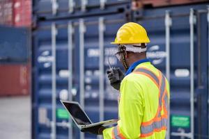 Arbeiter Mann im schützend Sicherheit Overall Uniform mit Gelb Helm und verwenden Walkie Talkie prüfen Container beim Ladung Versand Lagerhaus. Transport Import Export logistisch industriell Bedienung foto