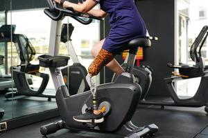 jung weiblich mit einer Prothese Bein mit ausüben mit ein Spinnen Fahrrad im das Fitnessstudio zu trainieren Joint verwenden mit das andere normal Bein zu Sein flexibel, Konzept von Leben ein Frau Leben mit ein Prothese foto