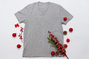 nahaufnahme graues leeres schablonen-t-shirt mit kopienraum und weihnachtsfeiertagskonzept. Draufsichtmodellt-shirt und rote Feiertagsdekorationen auf weißem Hintergrund. frohes neues jahr zubehör. Weihnachts-Outfit foto