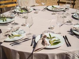 Hochzeit Bankett Konzept. Stühle und runden Tabelle zum Gäste, serviert mit Messerschmied Und, Blumen und Geschirr und bedeckt mit ein Tischdecke foto