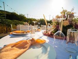 Hochzeit Bankett Konzept. Stühle und runden Tabelle zum Gäste, serviert mit Messerschmied Und, Blumen und Geschirr und bedeckt mit ein Tischdecke foto