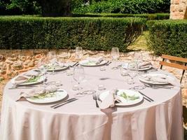 Hochzeit Bankett Konzept. Stühle und runden Tabelle zum Gäste, serviert mit Messerschmied Und, Blumen und Geschirr und bedeckt mit ein Tischdecke foto