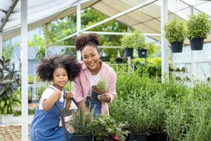 afrikanische mutter und tochter wählen gemüse- und kräuterpflanzen aus der örtlichen gärtnerei mit einkaufswagen voller sommerpflanzen für wochenendgarten und outdoor-konzept foto