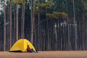 Solo über Nacht Camping während Sitzung neben Zelt beim Campingplatz im das Kiefer Wald während Schreiben Tagebuch zum Freiheit, Einsamkeit, friedlich Entspannung Flucht zu Wildnis und Natur Heilung Therapie foto