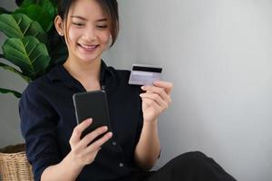 Frau, die auf ihrem Smartphone zahlt und eine Kreditkarte hält
